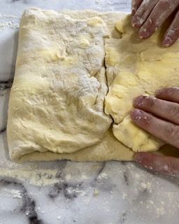 Una persona tiene in mano un pezzo di pasta su un tavolo.