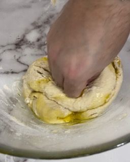Una persona sta impastando l'impasto in una ciotola di vetro.