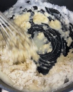 Un primo piano di una pastella in una padella con una frusta