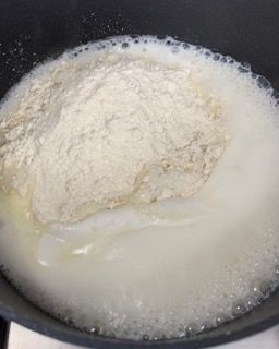 Primo piano di una pentola con latte e farina sul fornello.