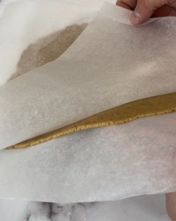 Una persona tiene un pezzo di carta oleata sopra un pezzo di pasta.