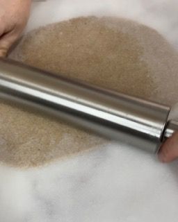 Una persona sta stendendo un pezzo di pasta con un mattarello.
