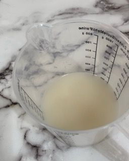Una tazza graduata piena di liquido bianco su una superficie di marmo