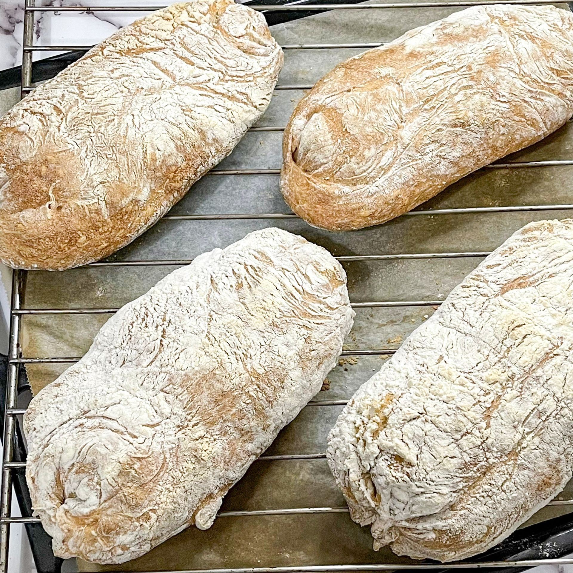 Quattro pagnotte di pane sono appoggiate su una griglia di raffreddamento.