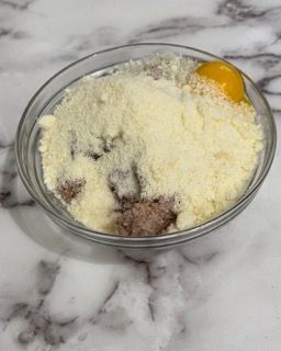 Una ciotola di vetro piena di formaggio in polvere, carne e un uovo.