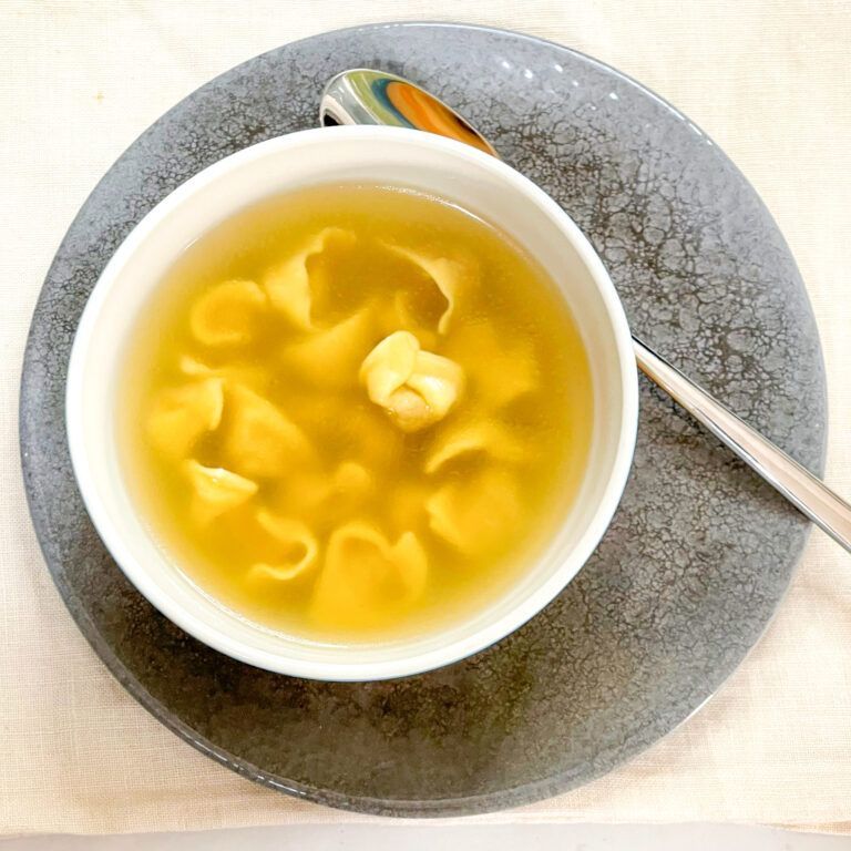 Una ciotola di zuppa con tagliatelle e un cucchiaio su un piatto.