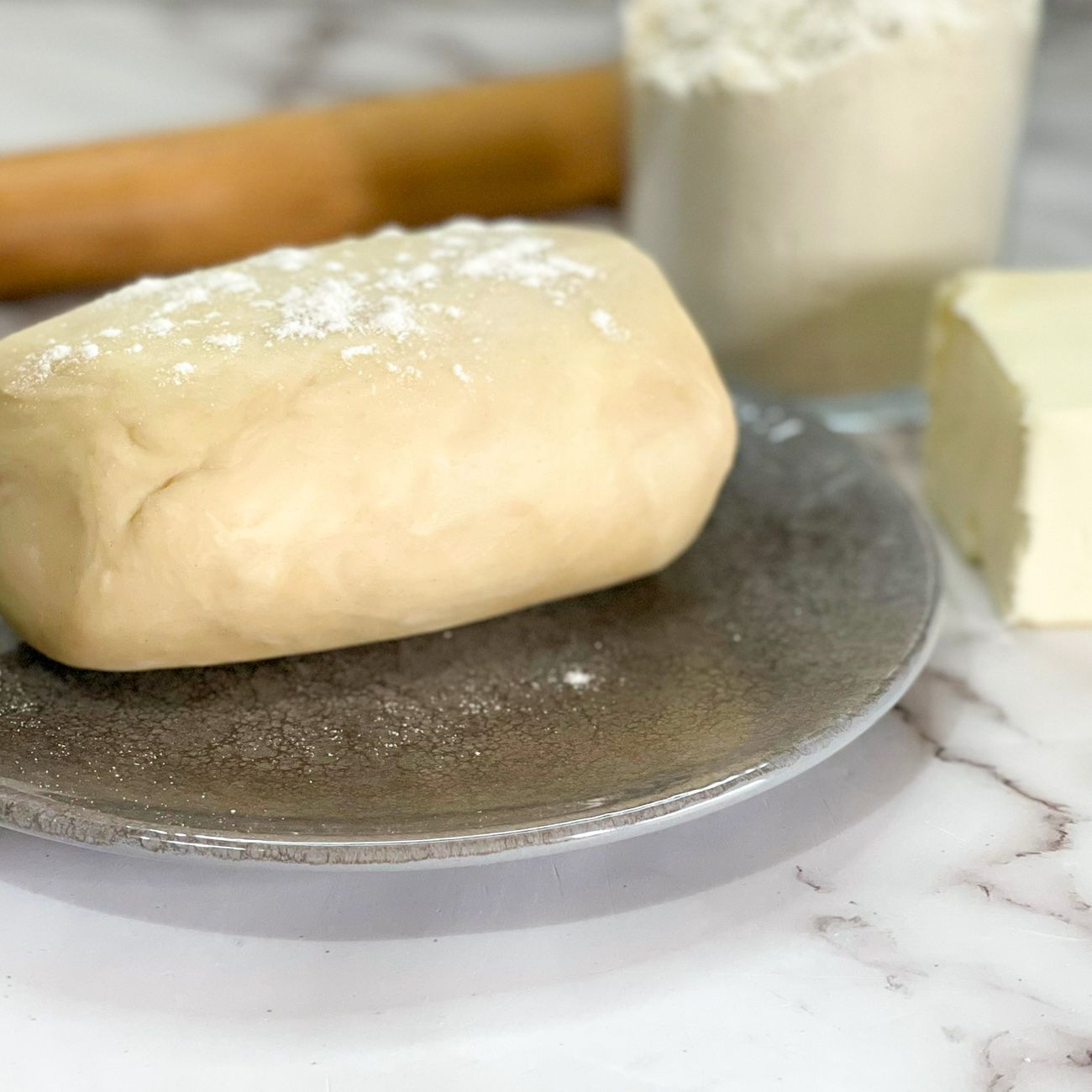 Un pezzo di pasta è appoggiato su un piatto accanto a un pezzetto di burro.