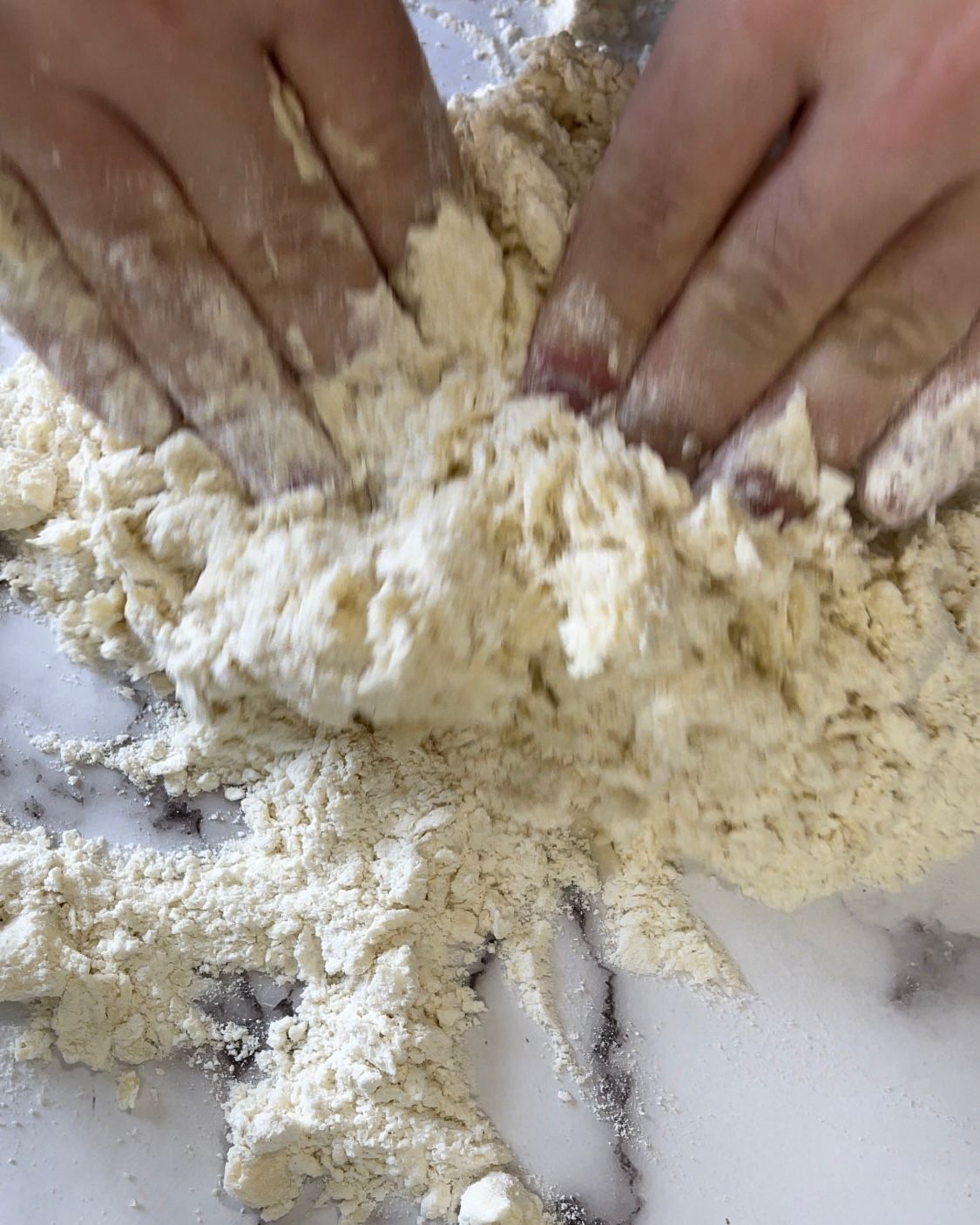 Le mani di una persona sono coperte di farina su un tavolo.