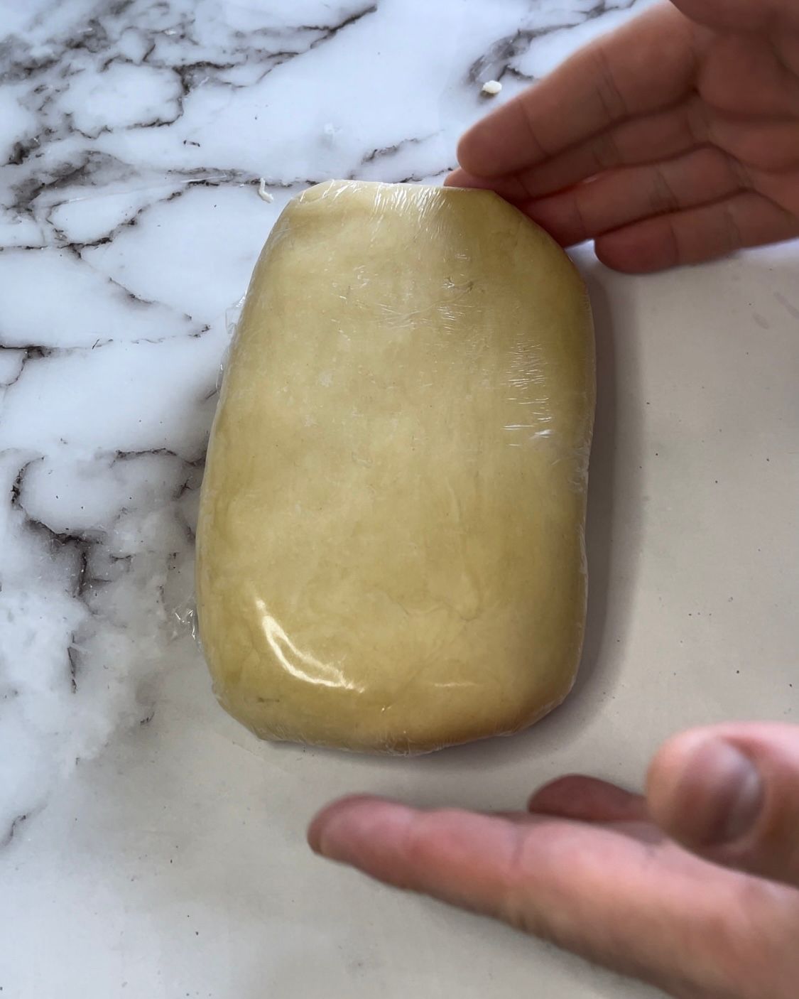 Una persona tiene in mano un pezzo di pasta su una superficie di marmo.