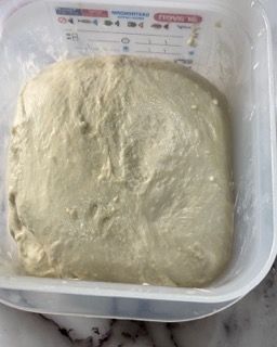 Un contenitore di plastica pieno di impasto è appoggiato su un tavolo.