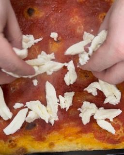 Una persona sta mettendo il formaggio su una pizza con salsa di pomodoro