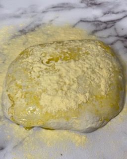 Una palla di pasta è ricoperta di farina su una superficie di marmo.