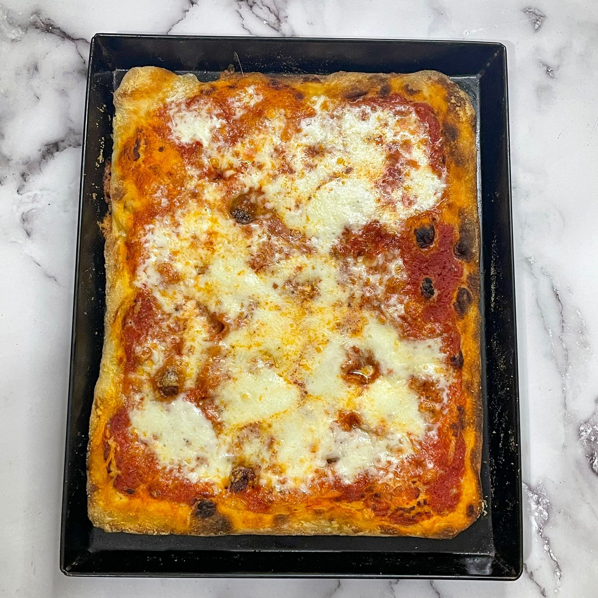 Una pizza con salsa di pomodoro e formaggio è in una padella nera su un tavolo.