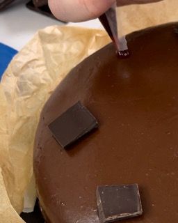 Una persona sta glassando una torta al cioccolato con una pipetta