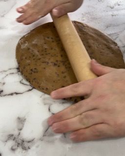 Una persona sta stendendo un pezzo di pasta con un mattarello.