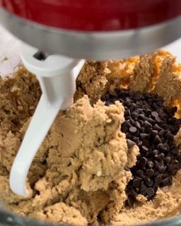 Un mixer mescola l'impasto dei biscotti e le gocce di cioccolato in una ciotola di vetro.