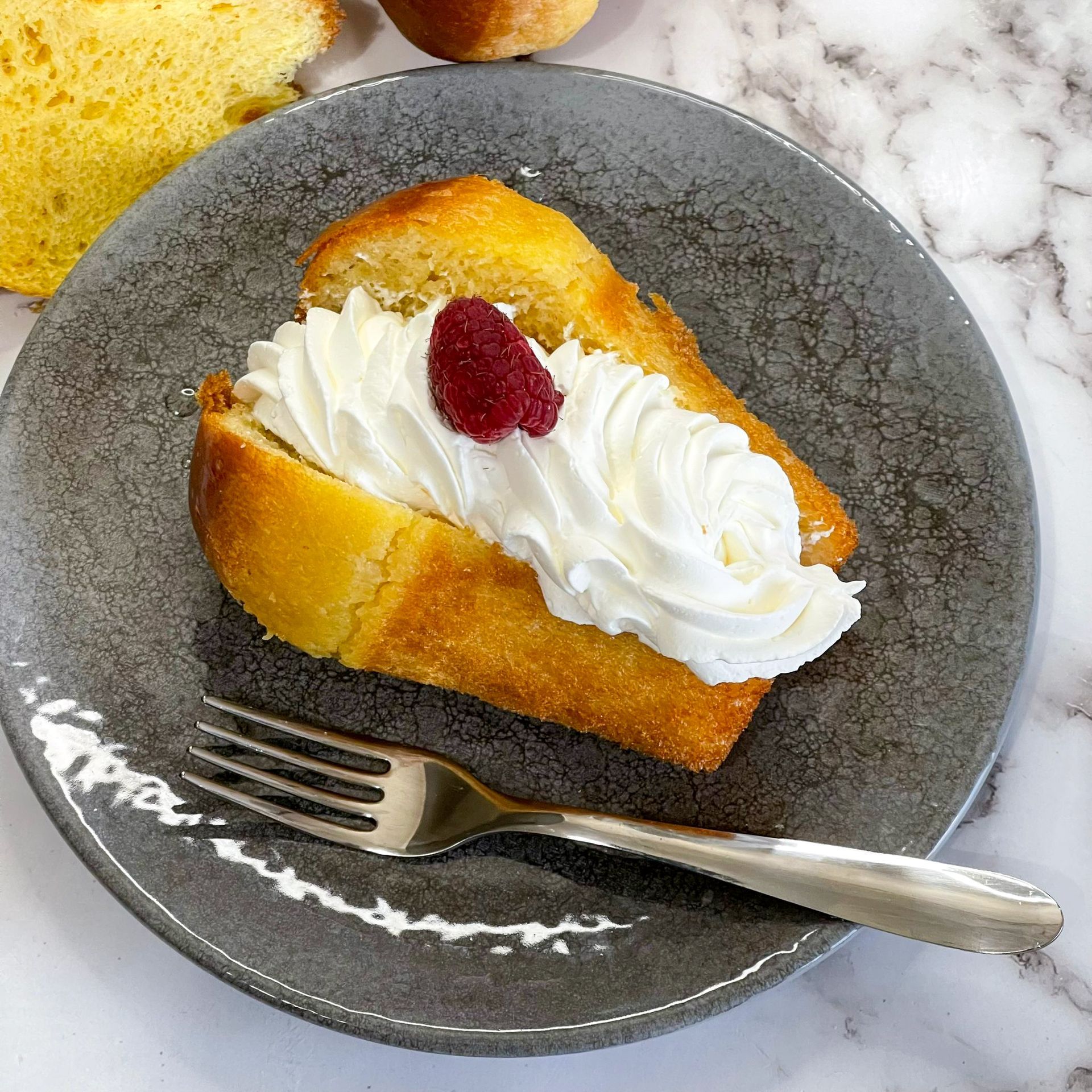 Una fetta di torta con panna montata e lamponi su un piatto con una forchetta.