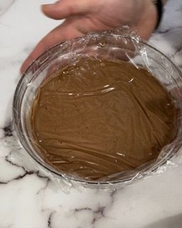 Una persona tiene in mano una ciotola di cioccolato ricoperta di pellicola trasparente.