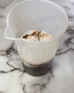 Un misurino pieno di liquido è appoggiato su un bancone di marmo.