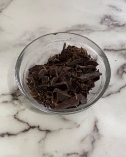 Una ciotola di vetro piena di cioccolato tritato su una superficie di marmo.