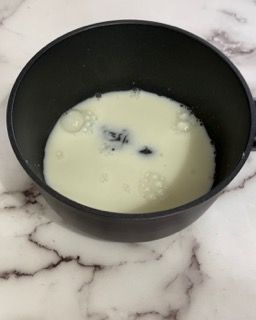 Una ciotola nera piena di liquido bianco su una superficie di marmo.