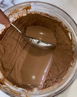 Una persona tiene in mano un cucchiaio in una ciotola di mousse al cioccolato.