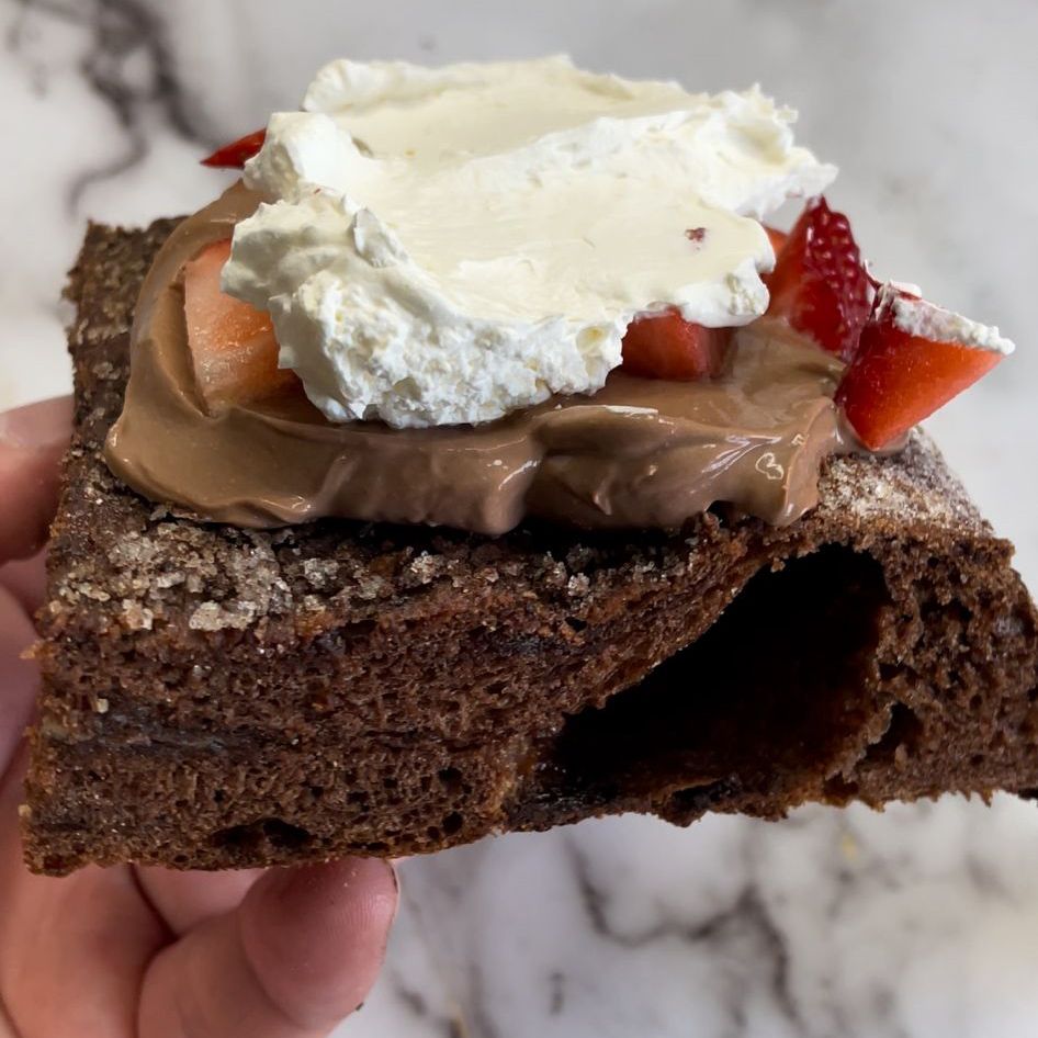 Una persona tiene in mano un pezzo di torta al cioccolato con panna montata e fragole sopra