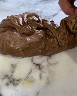 Una persona tiene in mano un pezzo di pasta al cioccolato su una superficie bianca.