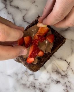 Una persona sta mettendo delle fragole sopra un brownie.