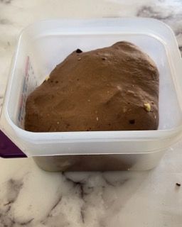 Un contenitore di plastica pieno di budino al cioccolato è appoggiato su un tavolo.