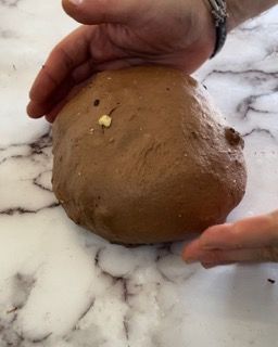 Una persona tiene in mano un pezzo di pasta al cioccolato su un tavolo.