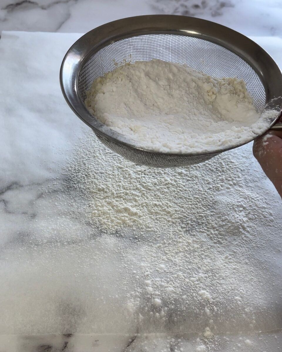 Una persona sta setacciando la farina in una ciotola su una superficie di marmo.
