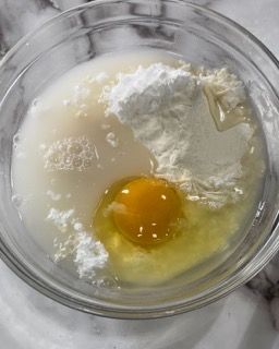 Una ciotola di vetro piena di uova, farina e liquido.