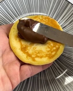 Una persona tiene in mano un pancake con sopra della crema al cioccolato