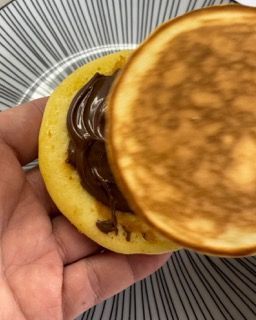 Una persona tiene in mano un pancake con sopra della crema al cioccolato