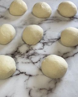 Un mucchio di palline di pasta sono appoggiate su una superficie di marmo.