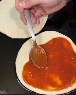 Una persona sta spalmando la salsa su una pizza con un cucchiaio