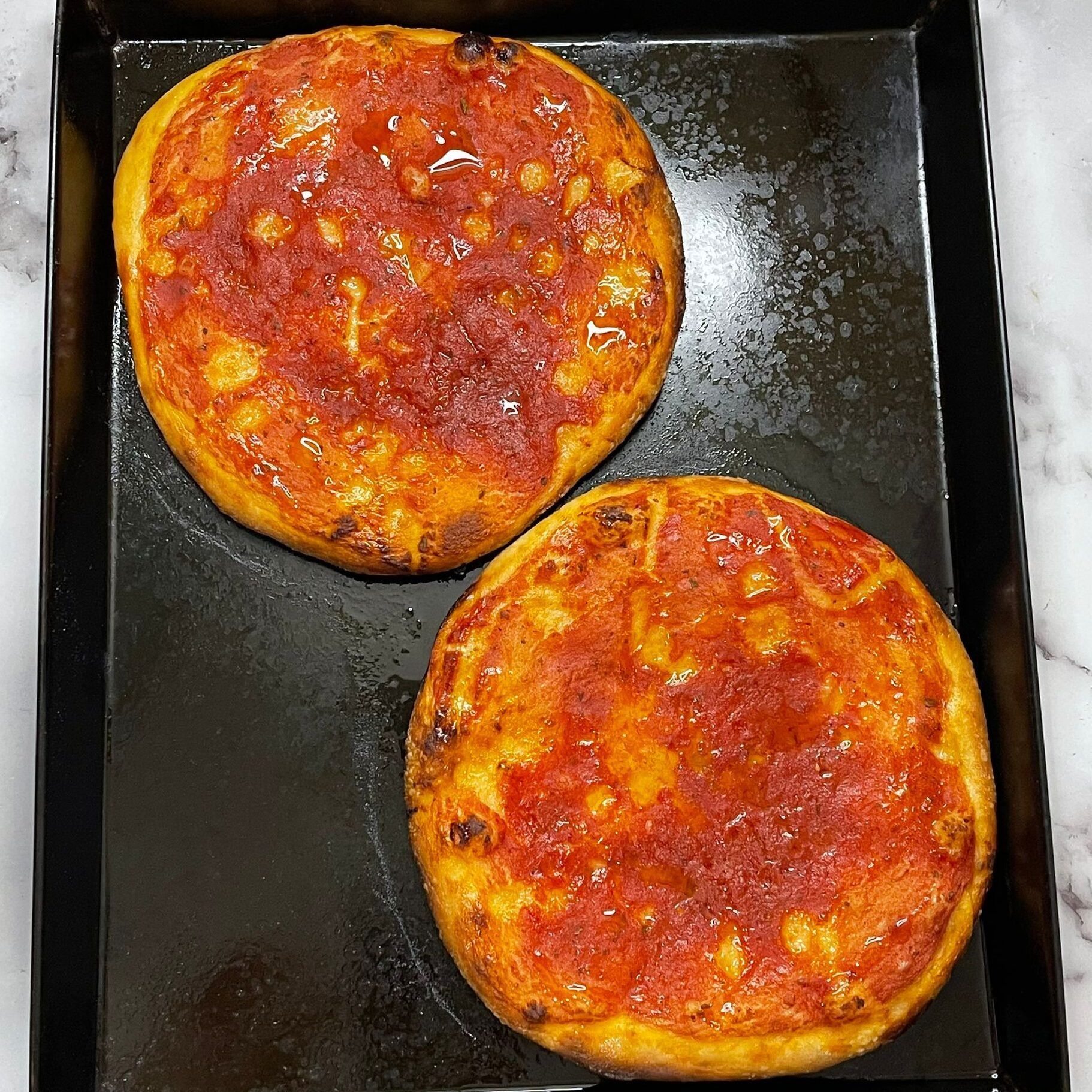 Due pizze sono appoggiate su un vassoio nero su un tavolo.