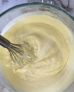 Si usa una frusta per mescolare un liquido giallo in una ciotola di vetro.