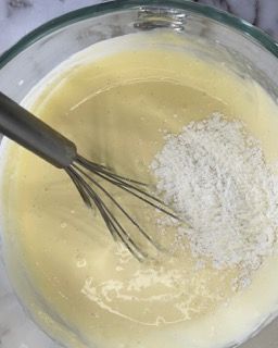 Una frusta è in una ciotola di pastella con farina.