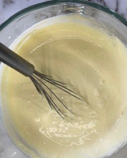 Si usa una frusta per mescolare un liquido giallo in una ciotola di vetro.