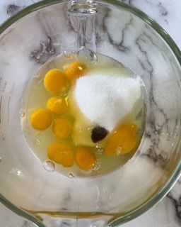 Un frullatore pieno di uova e zucchero su un tavolo.