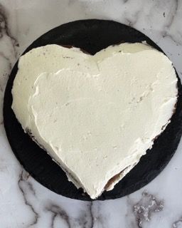 Una torta a forma di cuore con glassa bianca su un piatto nero