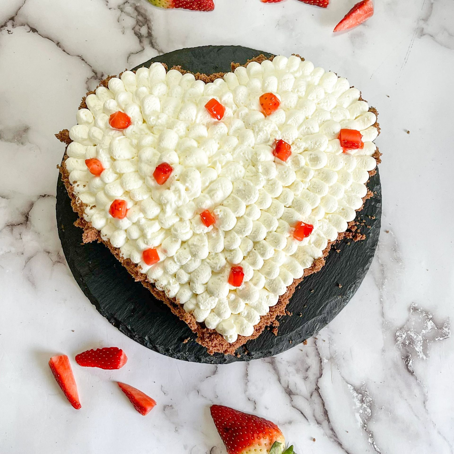 Una torta a forma di cuore con panna montata e fragole sopra.