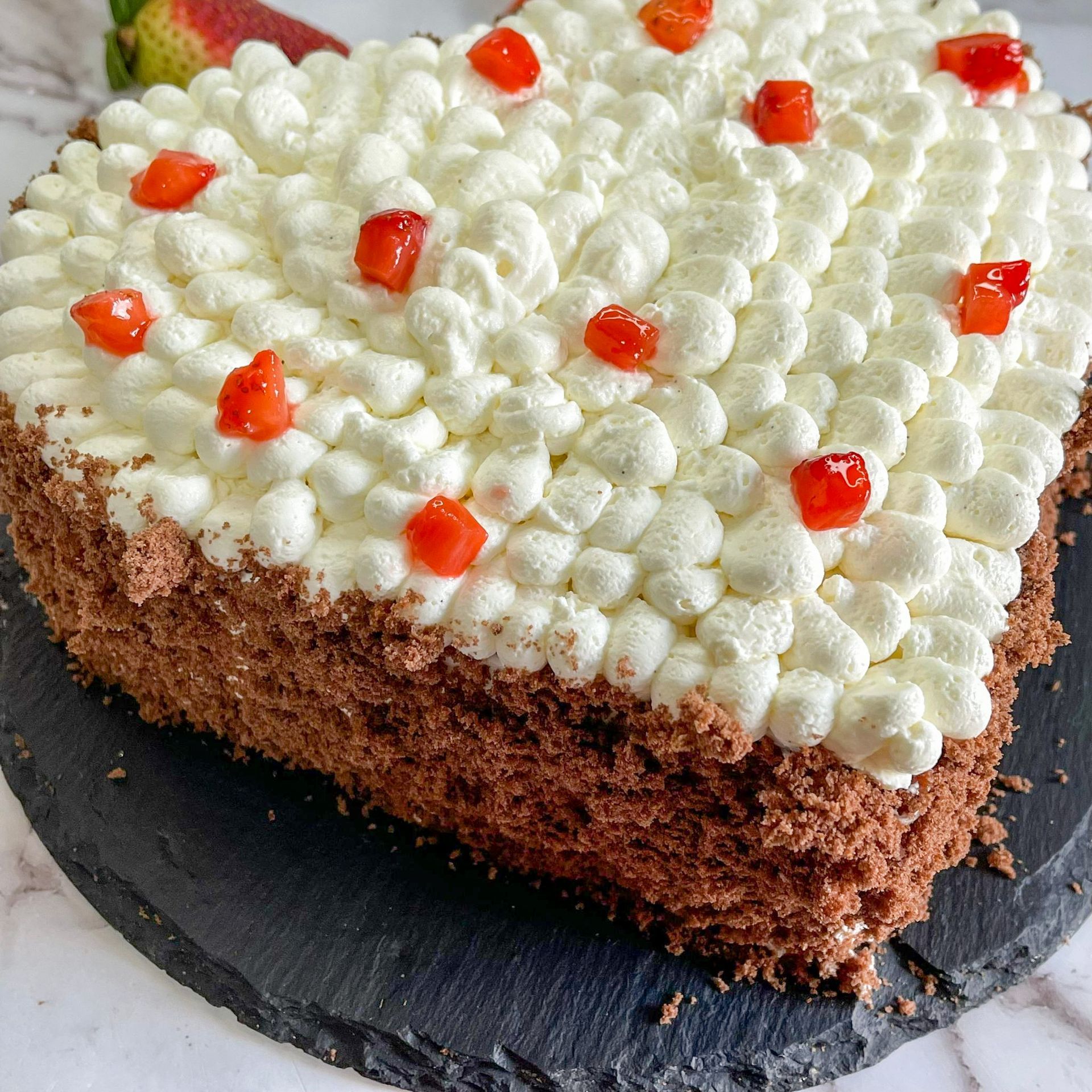 Una torta al cioccolato con panna montata e ciliegie sopra è servita su un piatto nero.