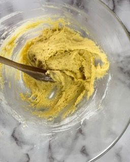Una ciotola di vetro piena di pastella gialla e un cucchiaio dentro.