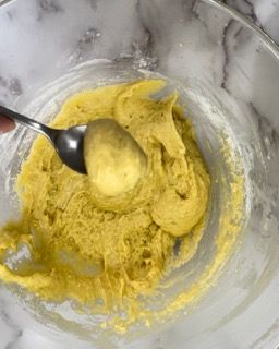Una persona tiene in mano un cucchiaio in una ciotola di salsa gialla.