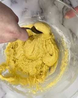 Una persona sta mescolando la pastella gialla in una ciotola con un cucchiaio.