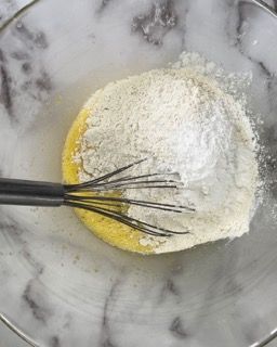 Una frusta è in una ciotola con farina e uovo.