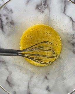 Una frusta è in una ciotola di uova su una superficie di marmo.